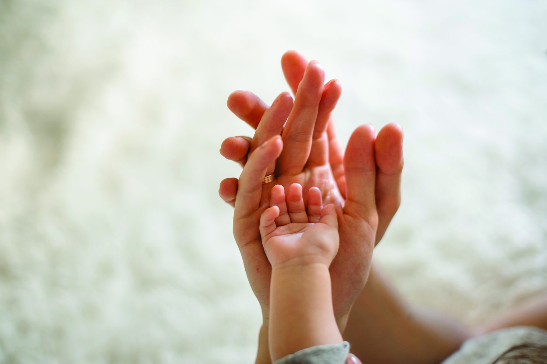 Close-up of a mother, father, and baby holding hands against the light-colored background of the room