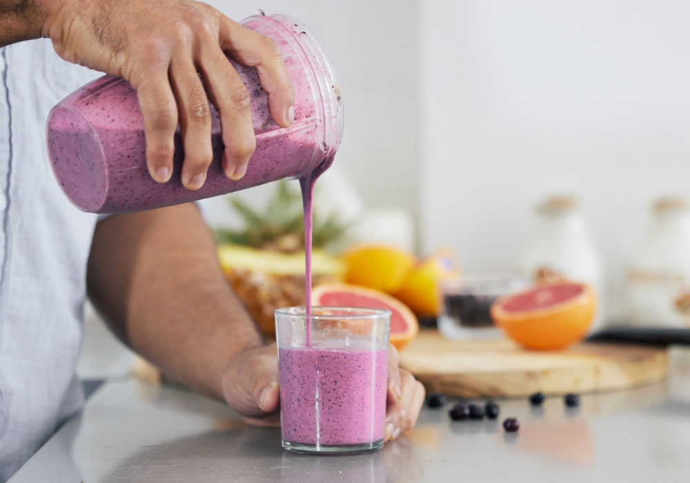 Man pouring a dark purple fruit shake into a glass