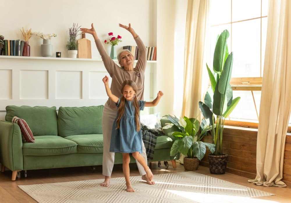 Großmutter, die mit ihrer Enkelin fröhlich und schwungvoll im Wohnzimmer tanzt